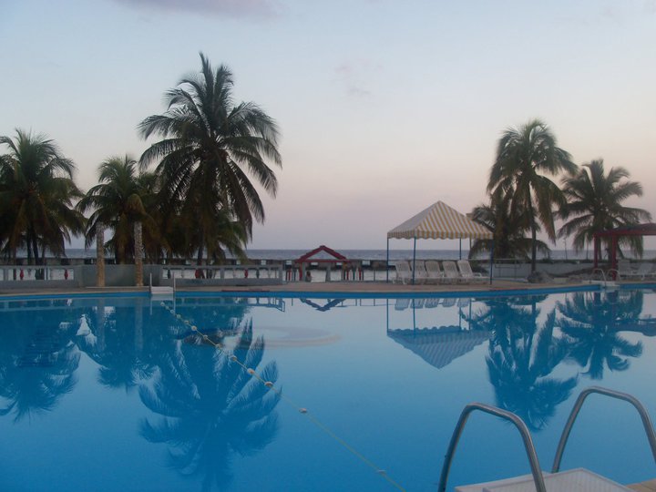 The sun sets over a swimming pool with palm trees