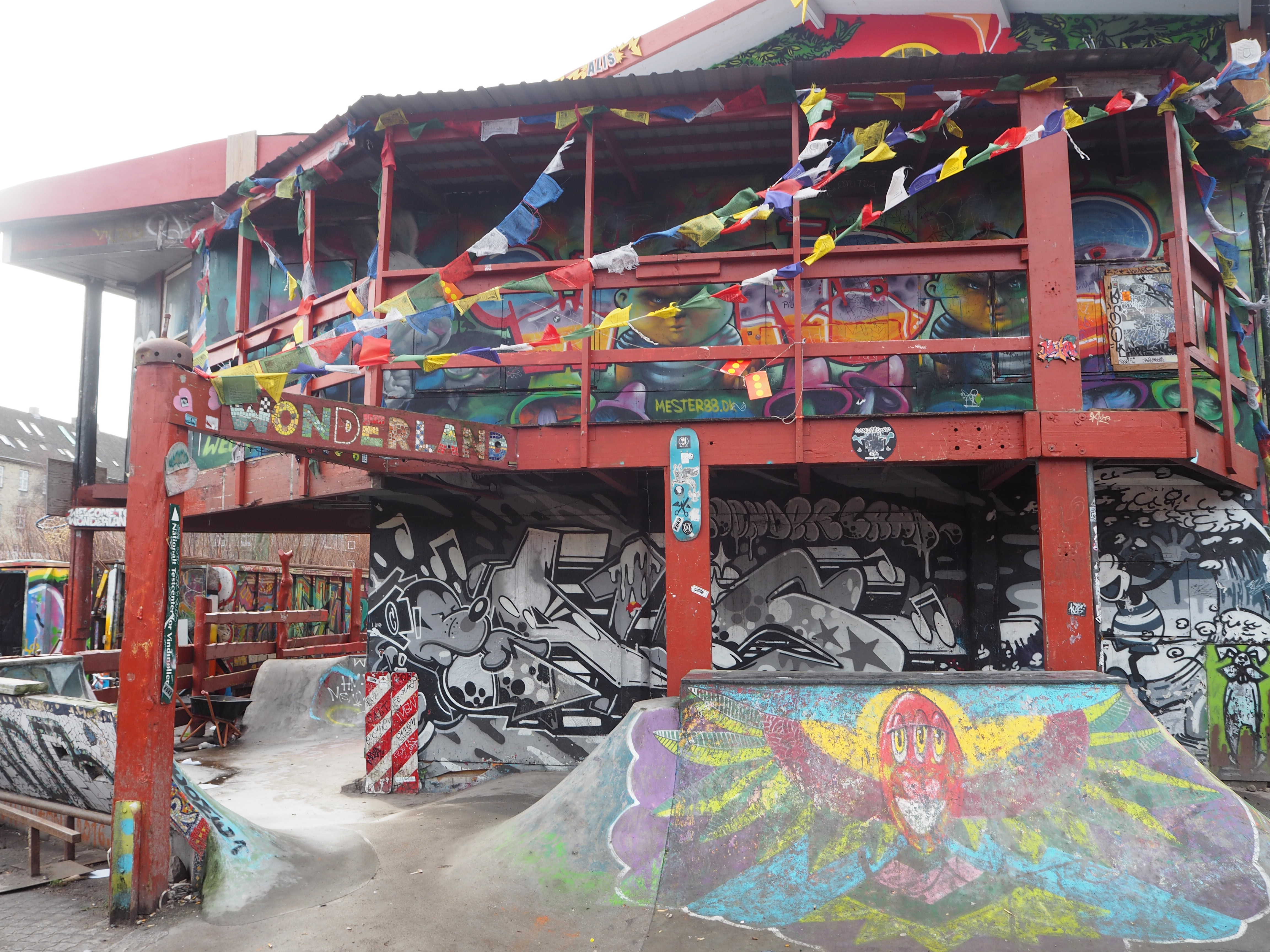 A large building covered in street art and flags stands inside a skate park in Freetown Christiana Copenhagen