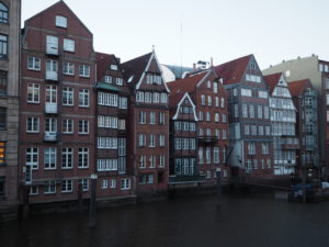 A row of tall, grey and brown houses with lots of windows, overlooking a river