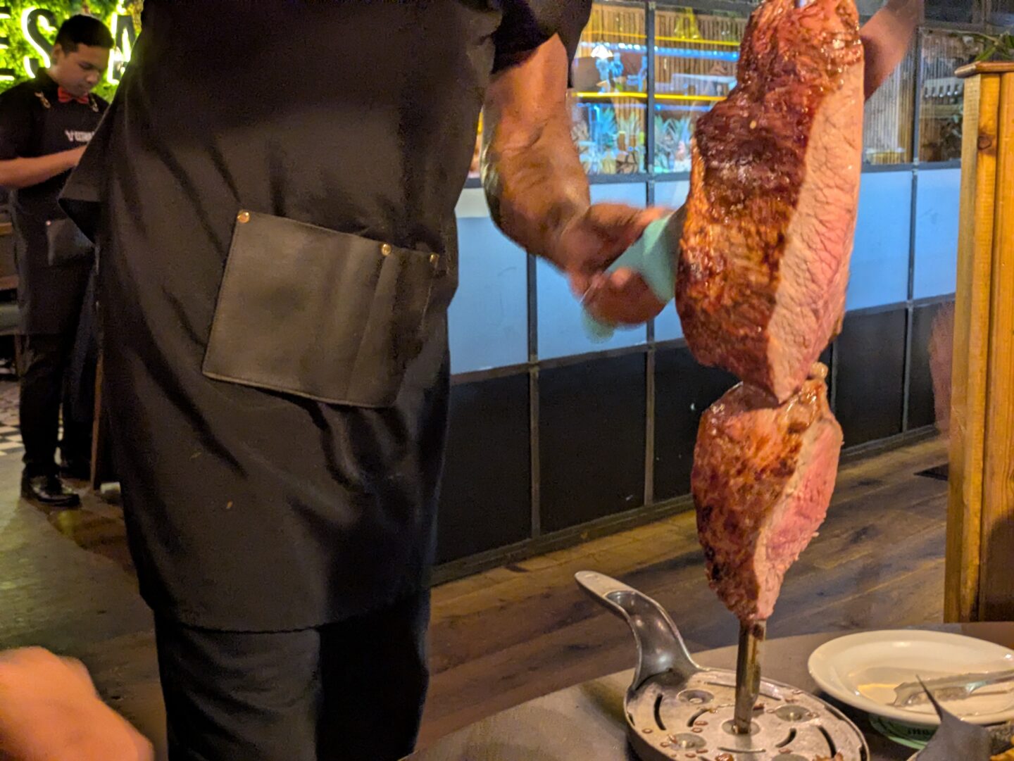 A large sirloin steak, with a waiter slicing a cut of the meat off